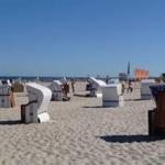Strand mit weißen Strandkörben und Menschen unter blauem Himmel.