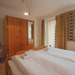 Schlafzimmer mit Doppelbett, Holzschrank und gelben Vorhängen.
