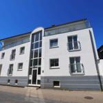 Moderne, mehrstöckige Wohnung mit Balkonen und Glasfassade unter blauem Himmel.