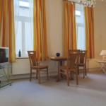 Wohnzimmer mit Esstisch, TV und Fenstern mit bunten Vorhängen.