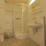 Badezimmer mit Dusche, Waschbecken und Toilette. Weiße Fliesen und Spiegelkabinett.