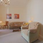Wohnzimmer mit Sofa, Sessel, Tisch und Wandbildern.