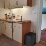 Küche mit Spüle, Kühlschrank und Kaffeemaschine. Blick in Wohnbereich mit Teppich.