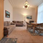 Wohnzimmer mit Sofa, Esstisch und Fenster. Deckenleuchte und Wandbilder.