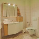 Badezimmer mit Waschbecken, Spiegel, Toilette und Dusche. Weiße Fliesen und Holzelemente.