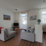 Wohnzimmer mit Sofa, Fernseher und Fenstern mit Vorhängen.