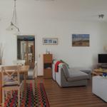 Wohn- und Essbereich mit Sofa, Tisch und Stühlen. Wandbild und TV sind sichtbar.