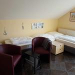 Zimmer mit zwei Betten, zwei roten Sesseln und einem Schrank. Wanddekoration und Fenster sichtbar.