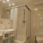 Badezimmer mit Dusche, Waschbecken und Toilette. Fliesen und Spiegel sichtbar.