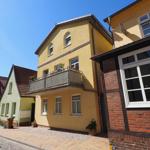 Gelbes Haus mit Balkon und Fenstern an einer Straße mit gepflastertem Gehweg.