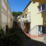 Hinterhof mit Treppe und Balkon an gelbem Haus mit Pflanzen und Steinplatten.