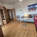 Wohnzimmer mit Sofa, Glas-Tisch und Holzboden. Wandbild zeigt Strand.