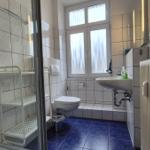 Badezimmer mit Dusche, Toilette und Waschbecken. Blaue Bodenfliesen und Fenster mit Vorhängen.