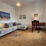 Wohnzimmer mit Sofa, Couchtisch und Schreibtisch. Holzboden und Wandbilder.