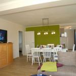 Wohn- und Essbereich mit grüner Wand, weißem Tisch und Sofa mit Kissen.