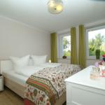 Schlafzimmer mit Doppelbett, grünen Vorhängen und Fensterblick auf Grünflächen.