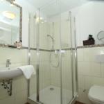 Badezimmer mit Dusche, Waschbecken und Toilette. Fliesen und Spiegel sichtbar.