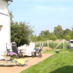 Terrasse mit Tisch, Stühlen und Liege. Grasfläche und Strandkorb im Hintergrund.