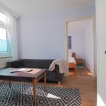 Wohnzimmer mit Sofa, Tisch und Blick in Schlafzimmer mit Bett.