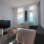 Wohnzimmer mit Sofa, Fernseher und Fenster mit Vorhängen.