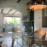 Dining area with glass table and wooden chairs. Kitchen and living area with view of green landscape.