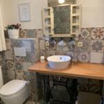 Bathroom with sink on sewing machine stand, colorful tiles, and mirror cabinet.