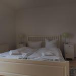 Schlafzimmer mit weißem Bett, zwei Nachttischen und grünen Lampen.