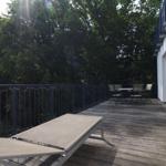 Terrasse mit Liegestuhl und Tischset vor grüner Baumreihe
