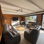Living room with sofa, armchair, TV, and view of balcony and landscape.