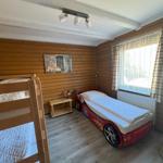 Room with bunk bed and race car bed, wooden walls and window with curtains.