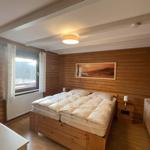 Bedroom with wood wall, double bed, crib, and window view.