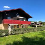 House with red balcony and green lawn under blue sky.