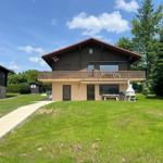 Wooden house with balcony, garden, and grill area under blue sky.
