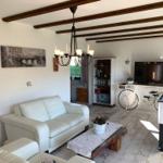 Living room with white sofa, table, and TV. Wooden beams on ceiling.