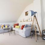 Zwei Sofas mit Kissen, Stehlampe, Tische und Wandbilder in einem Raum mit schräger Decke.