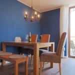 Esszimmer mit Holztisch, Stühlen und Bank. Blaue Wände und Glastür zum Balkon.
