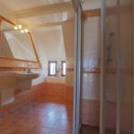 Badezimmer mit Dusche, Waschbecken und Heizung. Holzfenster und Kacheln.