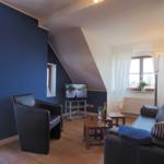 Wohnzimmer mit Sofa, Sessel, Fernseher und Fenster. Wand in Blau und Holzboden.