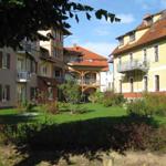 Hof mit mehreren Häusern, grüner Rasen und Bäumen im Hintergrund.