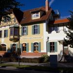 Historisches Gebäude mit Balkon und rotem Dach. Eingang mit Treppe und grünen Fensterläden.