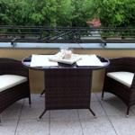 Terrasse mit runden Tisch und zwei Stühlen, weißer Sitzauflage, Tischdekoration und Blick auf Bäume.