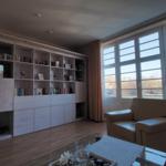 Wohnzimmer mit Bücherregal, Ledersofa und Glas-Tisch. Große Fenster mit Blick auf Balkon.