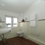 Badezimmer mit Waschbecken, Toilette und Heizkörper. Fenster mit Blick auf Landschaft.