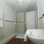 Badezimmer mit Dusche, Waschbecken und Heizkörper. Holzfußboden und weiße Wände.
