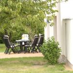 Terrasse mit Tisch und Stühlen unter Bäumen neben weißem Haus