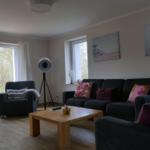 Wohnzimmer mit Sofa, Sessel und Holztisch. Fenster und Wandbilder sichtbar.
