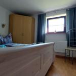 Schlafzimmer mit Bett, Kleiderschrank und Fenster mit Vorhängen.