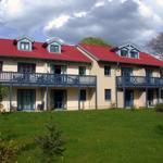Zweistöckiges Haus mit rotem Dach und blauen Balkonen auf grünem Grundstück.