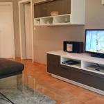 Wohnzimmer mit Sofa, Glas-Tisch und TV auf weißen Schränken.