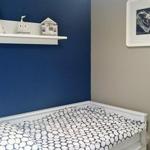 Ein Bett mit gemusterter Bettwäsche, blaue Wand, weiße Regal mit Dekoration und Wandbild.